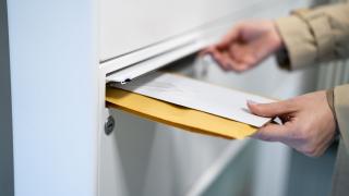 Ihminen tiputtaa kirjekuoria postilaatikkoon.