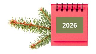 Vihreän kuusenhavun päällä on punainen vuosikalenteri 2026.