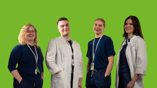 VAKEn kaksi sairaanhoitajaa ja kasi lääkäriä poseeraavat kuvassa työasuissaan, vihreää taustaa vasten.